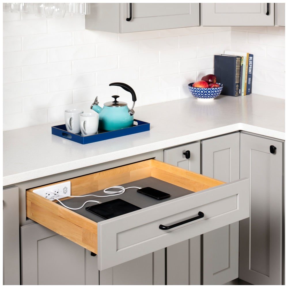 Charging drawer open in a kitchen base cabinet, phones and tablet charging inside