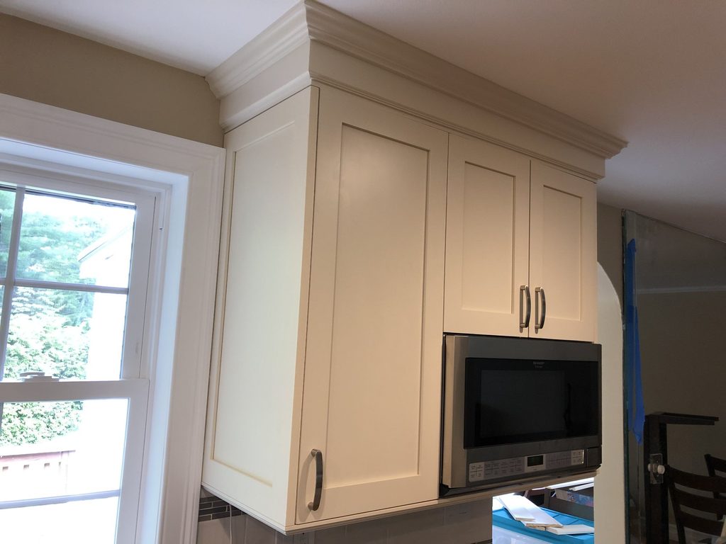 Integrated over-the-counter microwave set into cream wall cabinets beside a window