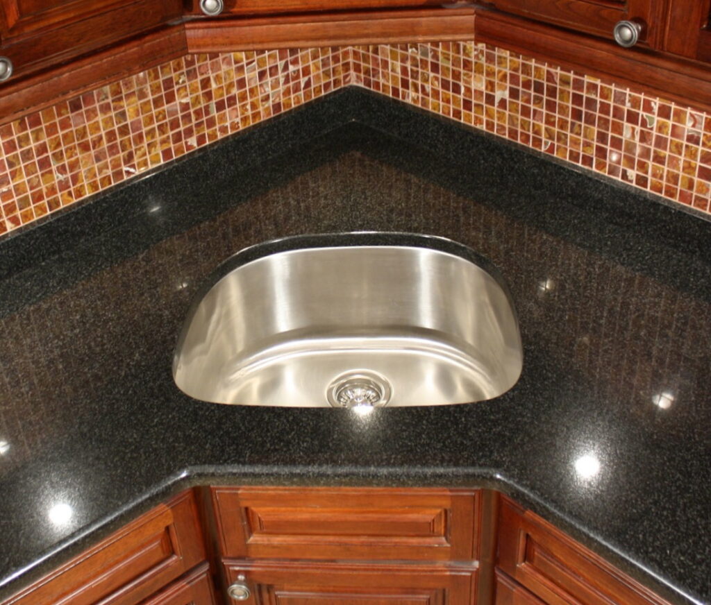 D-bowl stainless steel sink installed in a corner sink cabinet with a dark granite countertop