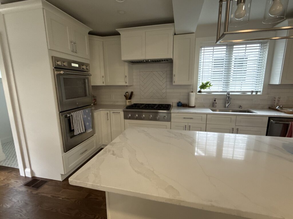 Double wall ovens in tall white cabinetry beside the quartz island – West Roxbury