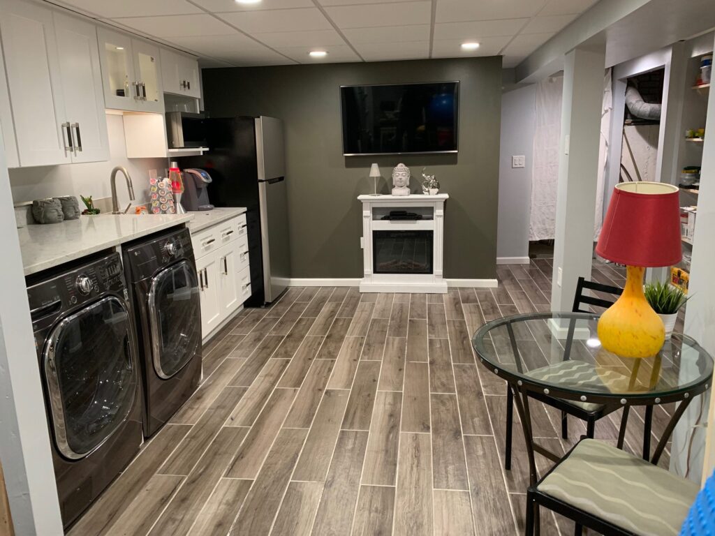 Wide view of the finished basement with kitchenette and wood-look tile floor – Randolph